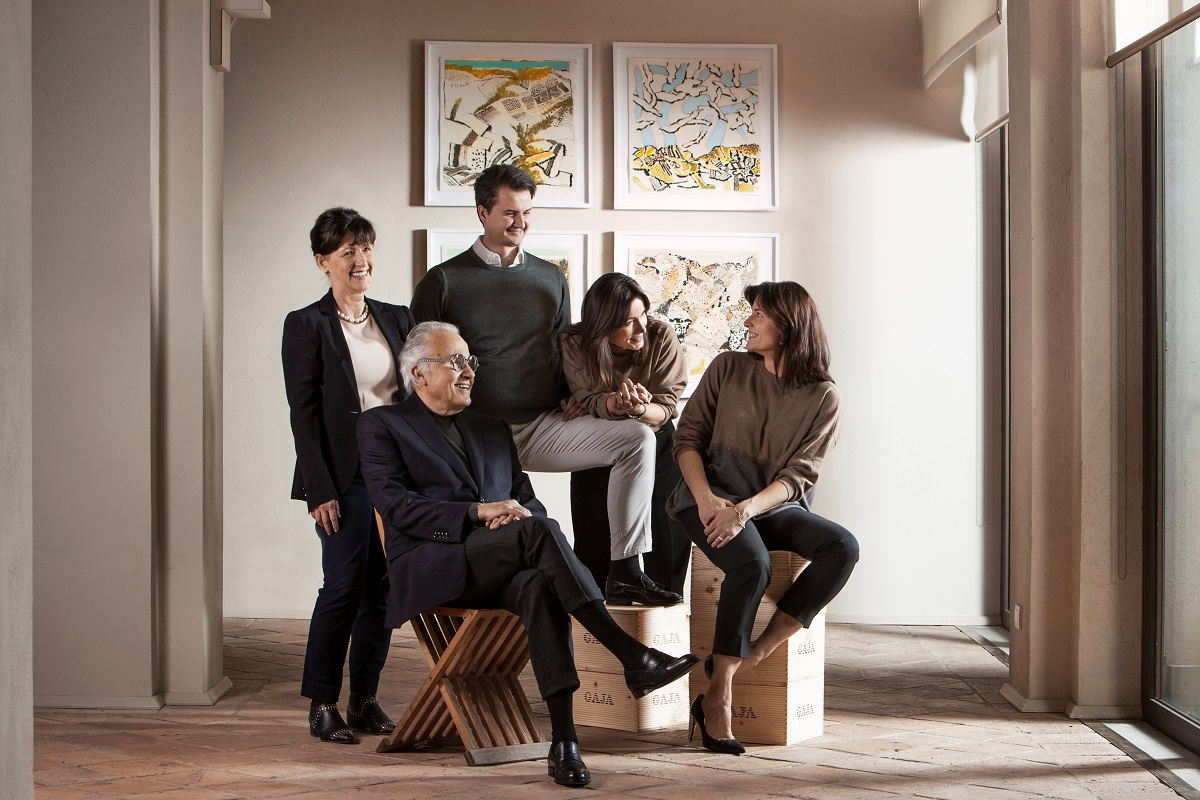 Eine Gruppe von fünf Personen posiert in einem hellen Raum mit Kunstwerken an der Wand. Ein älterer Mann sitzt auf einem stilisierten Stuhl, während die anderen um ihn herum stehen und sitzen.