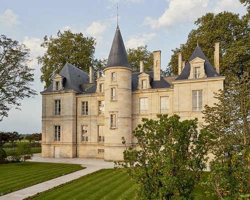 Ein elegantes Schloss mit Türmen und symmetrischen Fenstern steht in einer grünen Umgebung. Der gepflegte Garten und die Bäume umgeben das Gebäude, während der Himmel leicht bewölkt ist.