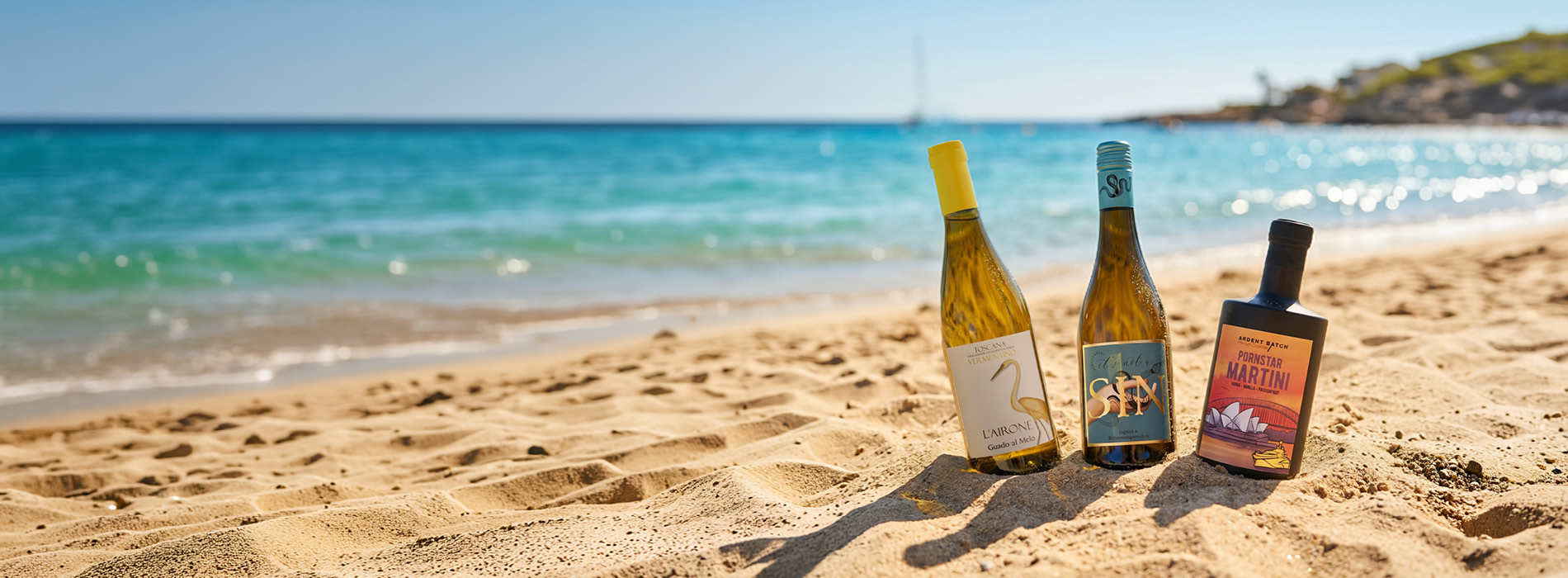 Drei Flaschen Wein stehen im Sand am Strand. Im Hintergrund ist das glitzernde Wasser des Meeres und ein klarer Himmel zu sehen, was eine entspannte Urlaubsatmosphäre schafft.